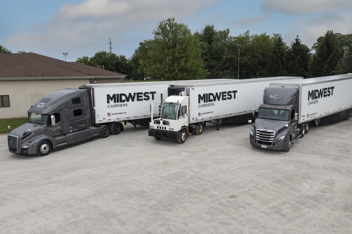 Three Midwest Carriers trucks parked in a lot with tree line in the background