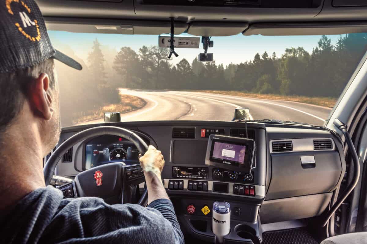 Man wearing a Midwest Carriers hat driving a truck down a curved road
