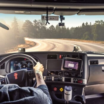 Man wearing a Midwest Carriers hat driving a truck down a curved road