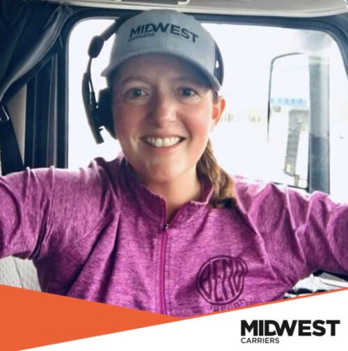 Female truck driver in purple jacket smiling in cab
